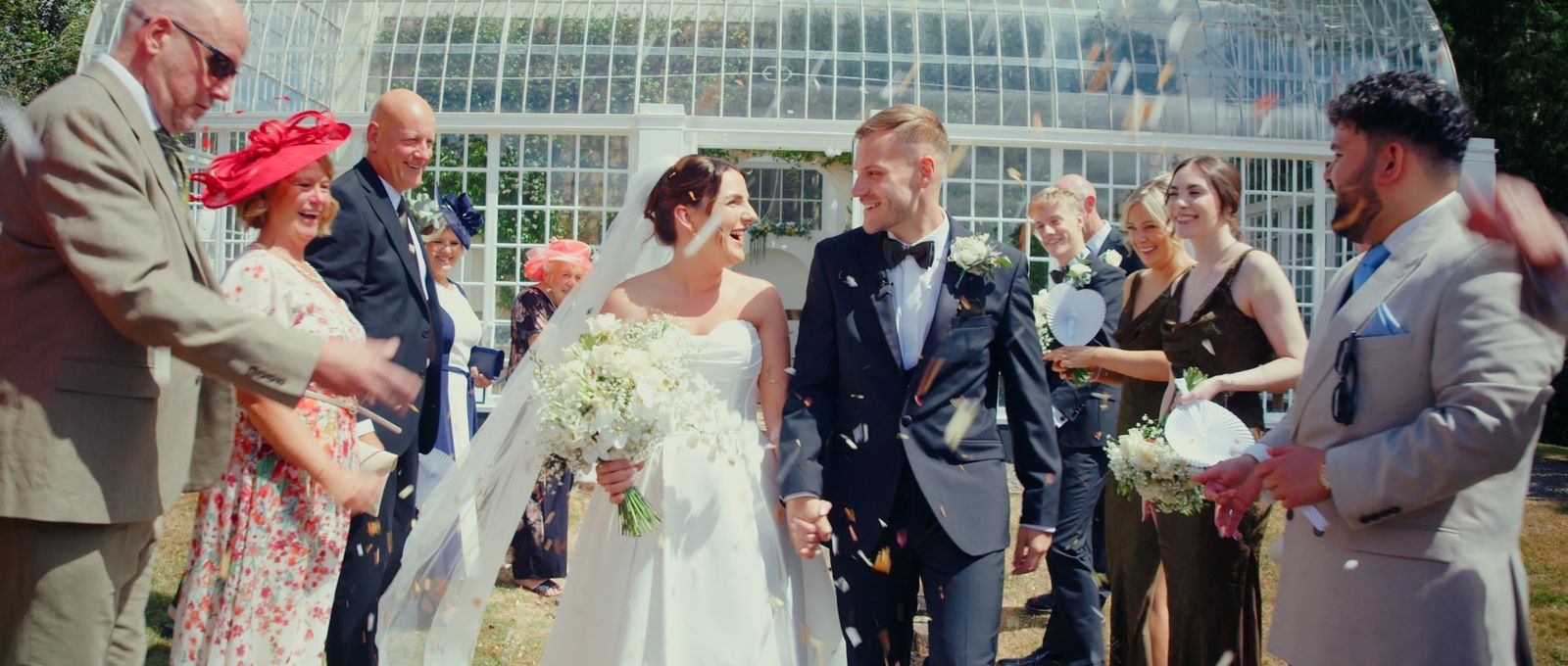 Tegan and Sam walking through a shower of confetti outside a glass orangery, surrounded by laughing guests