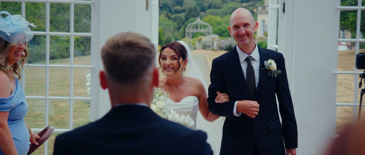 The bride arriving on her dad's arm, both beaming