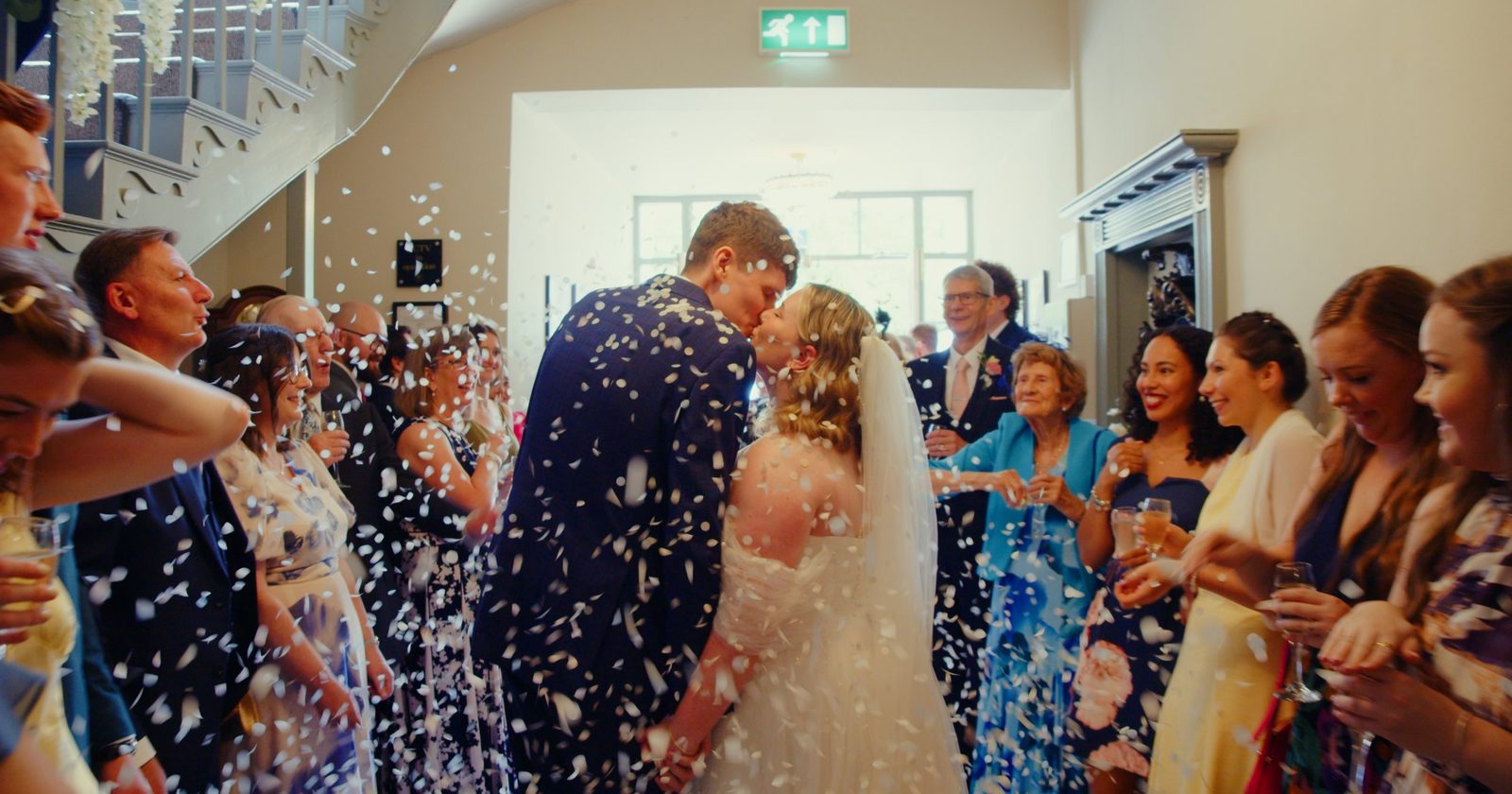Ellie and Chris kissing under a shower of white confetti as guests cheer either side