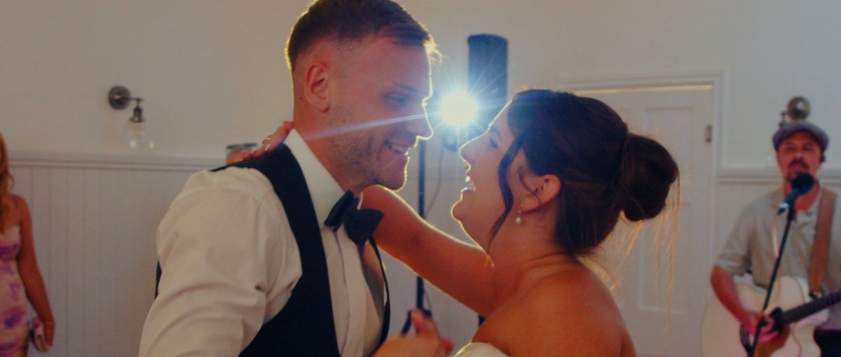 The couple smiling face to face during the first dance, a light flaring between them