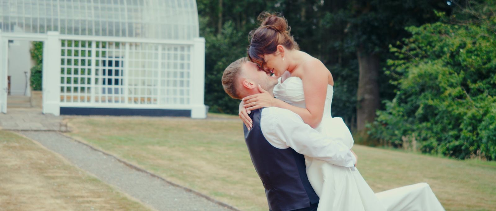 The groom lifting the bride for a kiss beside the orangery