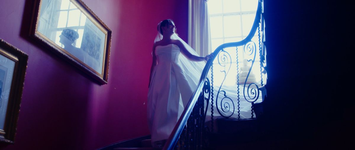 The bride coming down a sweeping staircase in a deep red hallway